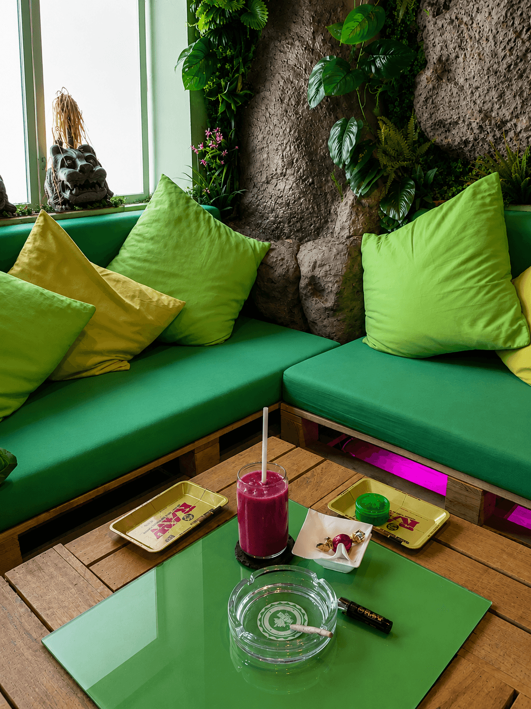 Zona lounge interior con sofás verdes y plantas tropicales en The Jungle, club privado de cannabis cerca del Parque del Retiro, Madrid